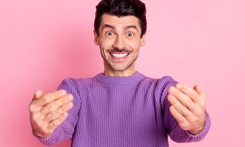 A photo of a man in a purple jersey in front of a pink background gesturing ‘bring it on’ with his hands